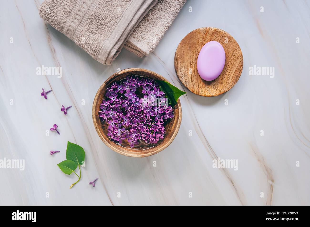 Composizione spa e benessere con fiori lilla profumati acqua in una ciotola di legno, asciugamani in spugna e sapone fatto a mano su sfondo in marmo. Aromaterapia, top Foto Stock