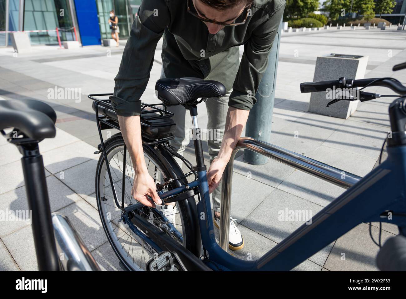 un giovane uomo d'affari guida una bicicletta elettrica mentre si dirige verso la torre dove si trova il suo ufficio Foto Stock