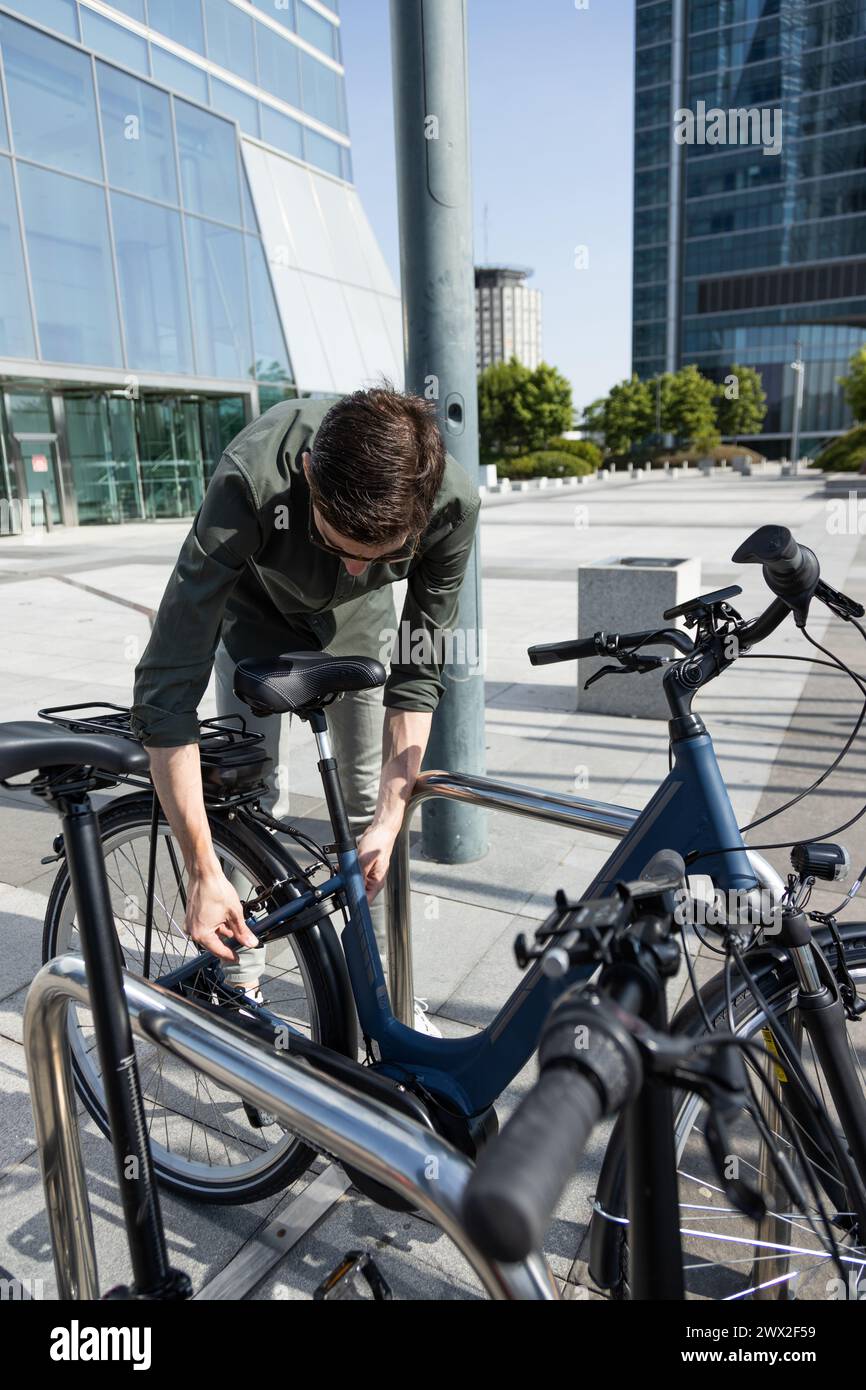 un giovane uomo d'affari guida una bicicletta elettrica mentre si dirige verso la torre dove si trova il suo ufficio Foto Stock
