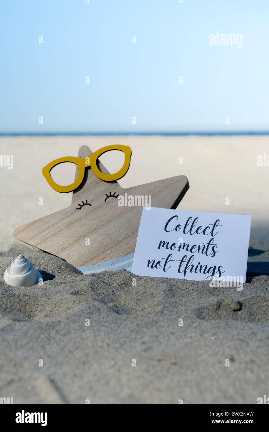 RACCOGLIERE MOMENTI NON COSE testo su carta biglietto di auguri sullo sfondo di divertente stella marina in occhiali decorazione vacanza estate. Spiaggia di sabbia costa sole. Rallentare, godersi il momento, momenti buoni, slow life concetto di vacanza cartolina. Un concetto di viaggio d'affari Foto Stock