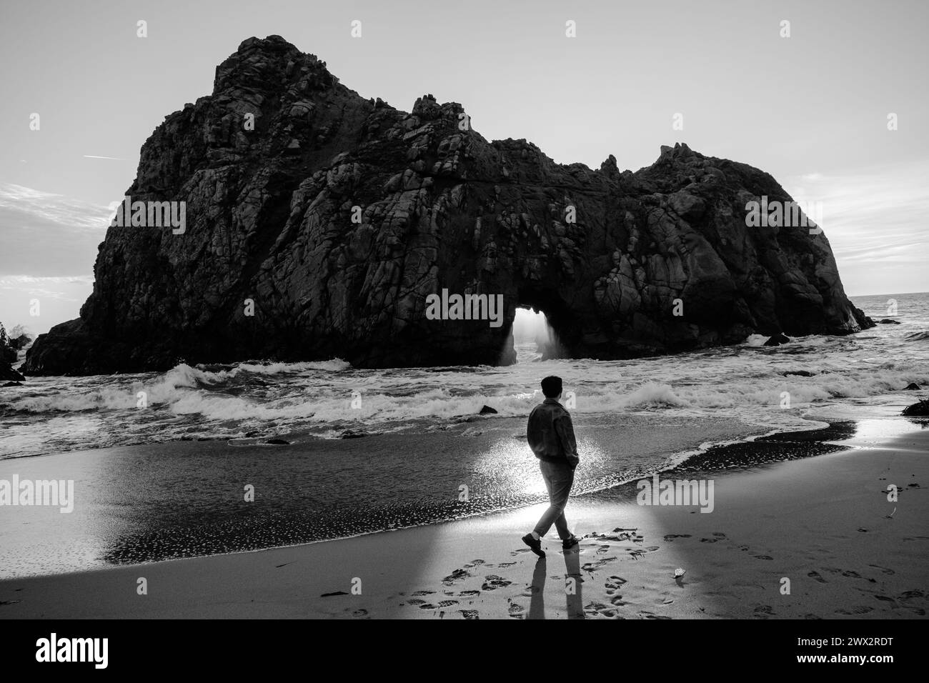 Il tramonto illumina la persona di fronte alla caratteristica Window in the Rock di Keyhole Arch a Pfeiffer Beach a Big Sur sull'Oceano Pacifico in California, Stati Uniti. Foto Stock