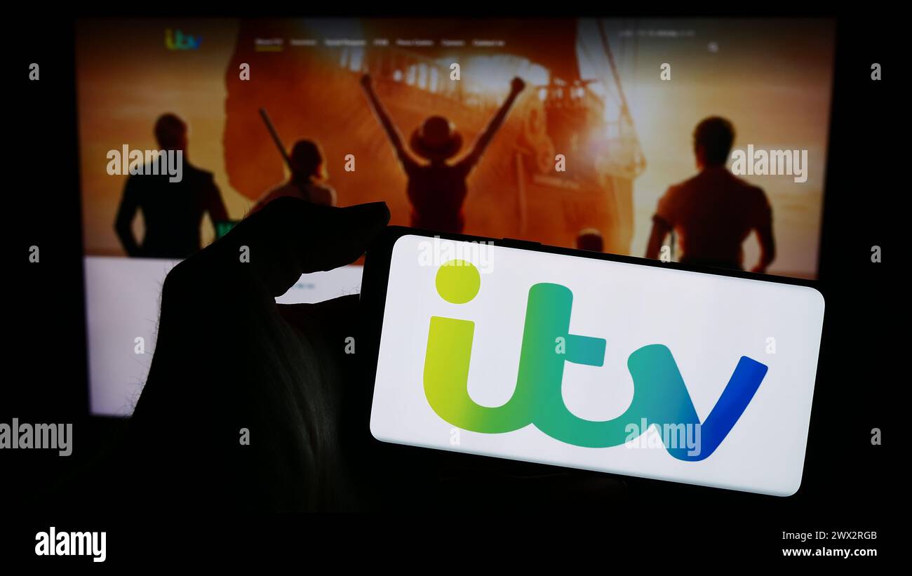 Persona che possiede uno smartphone con il logo della società britannica ITV plc di media e di radiodiffusione davanti al sito web. Mettere a fuoco il display del telefono. Foto Stock