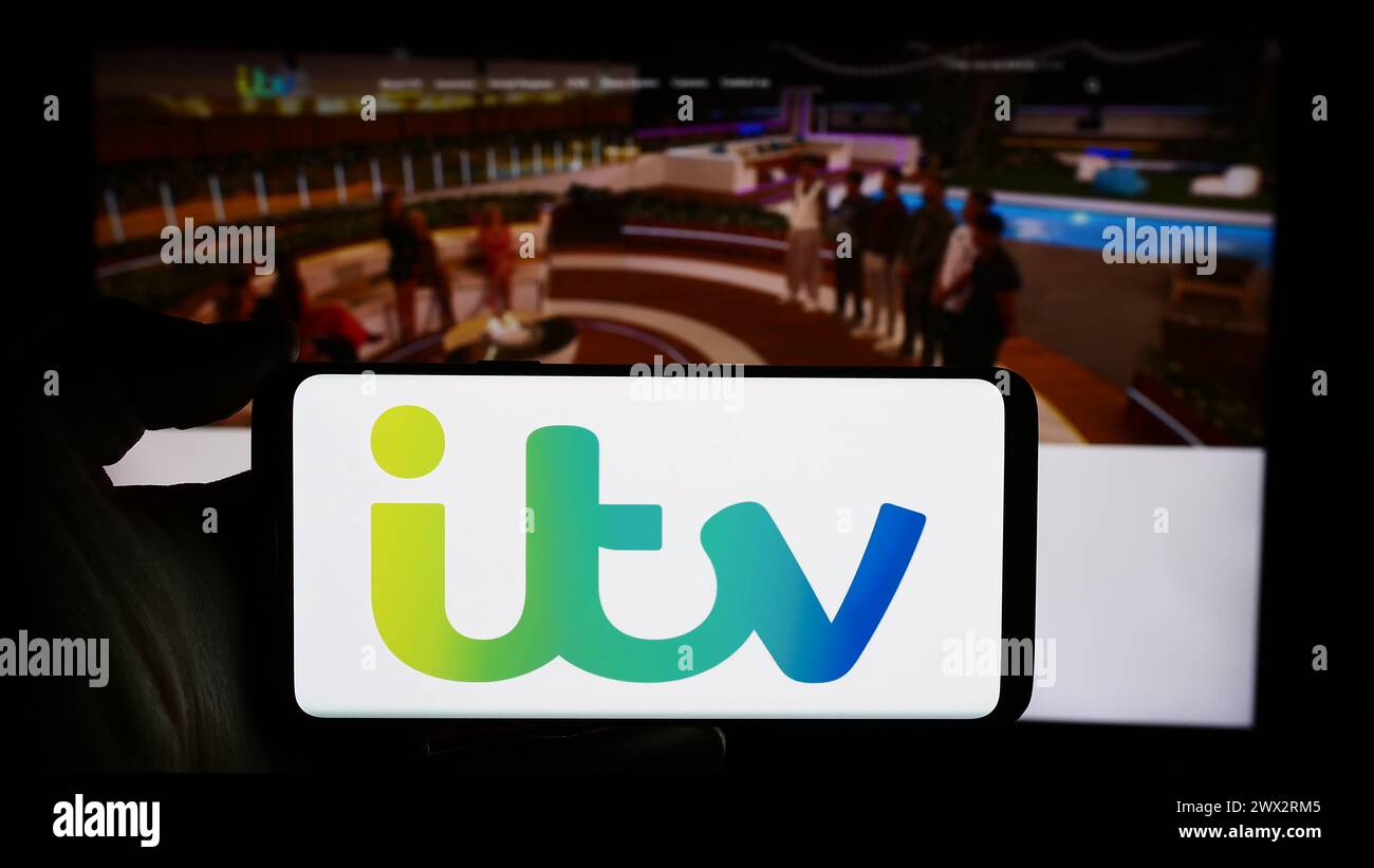 Persona che detiene un cellulare con il logo della società britannica ITV plc di stampa e di radiodiffusione di fronte alla pagina web aziendale. Mettere a fuoco il display del telefono. Foto Stock