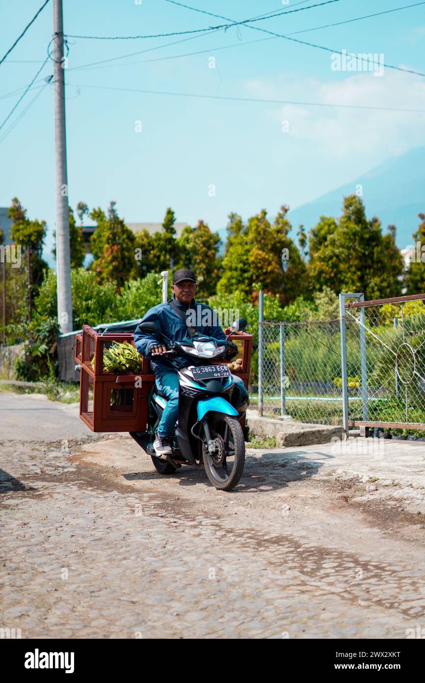 Un uomo che vende frutta usa una moto durante il giorno con alberi e montagne sullo sfondo Foto Stock