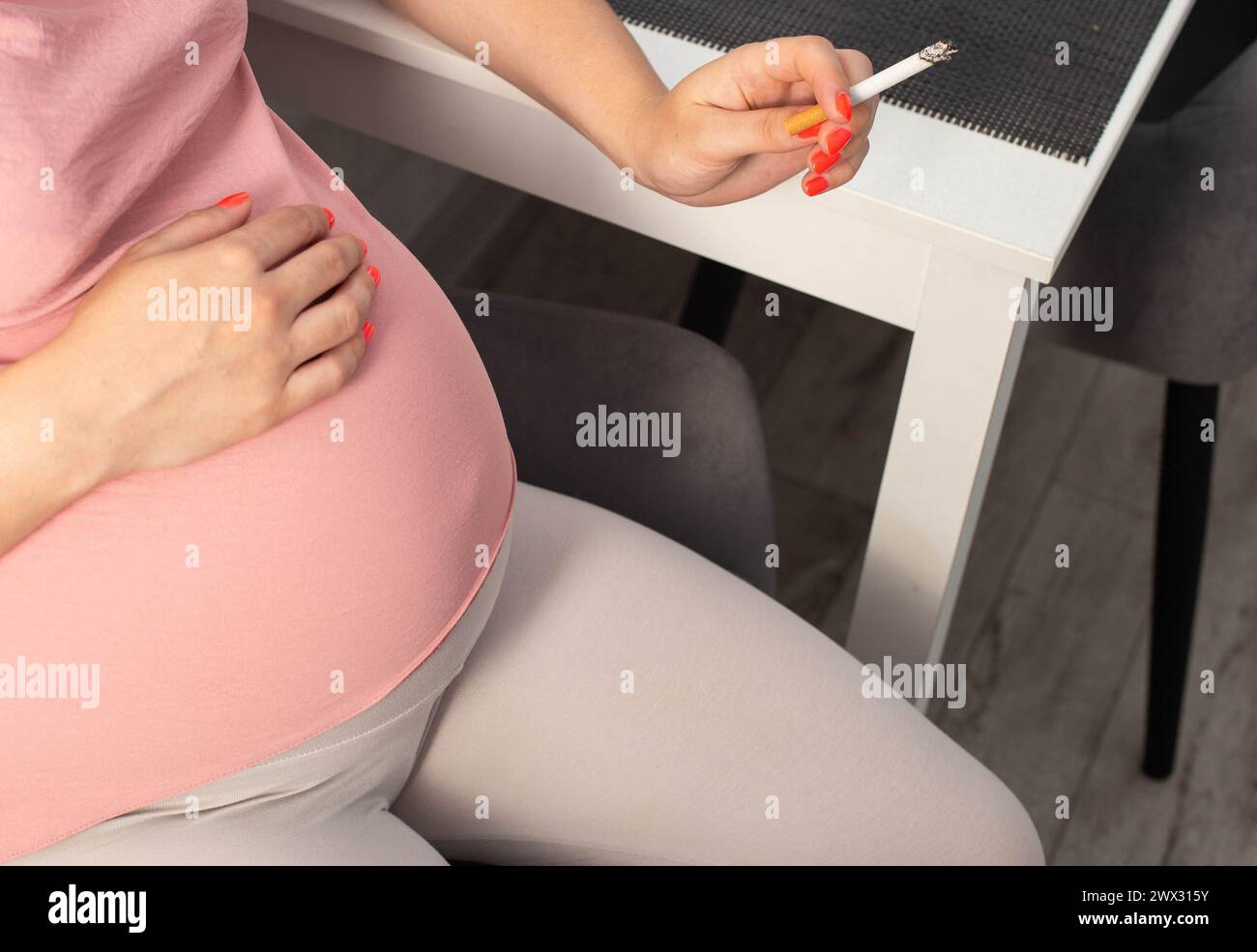 Una ragazza incinta con una grande pancia tiene una sigaretta in mano. Fumare durante la gravidanza. Danno alla salute della madre e del bambino. Foto Stock