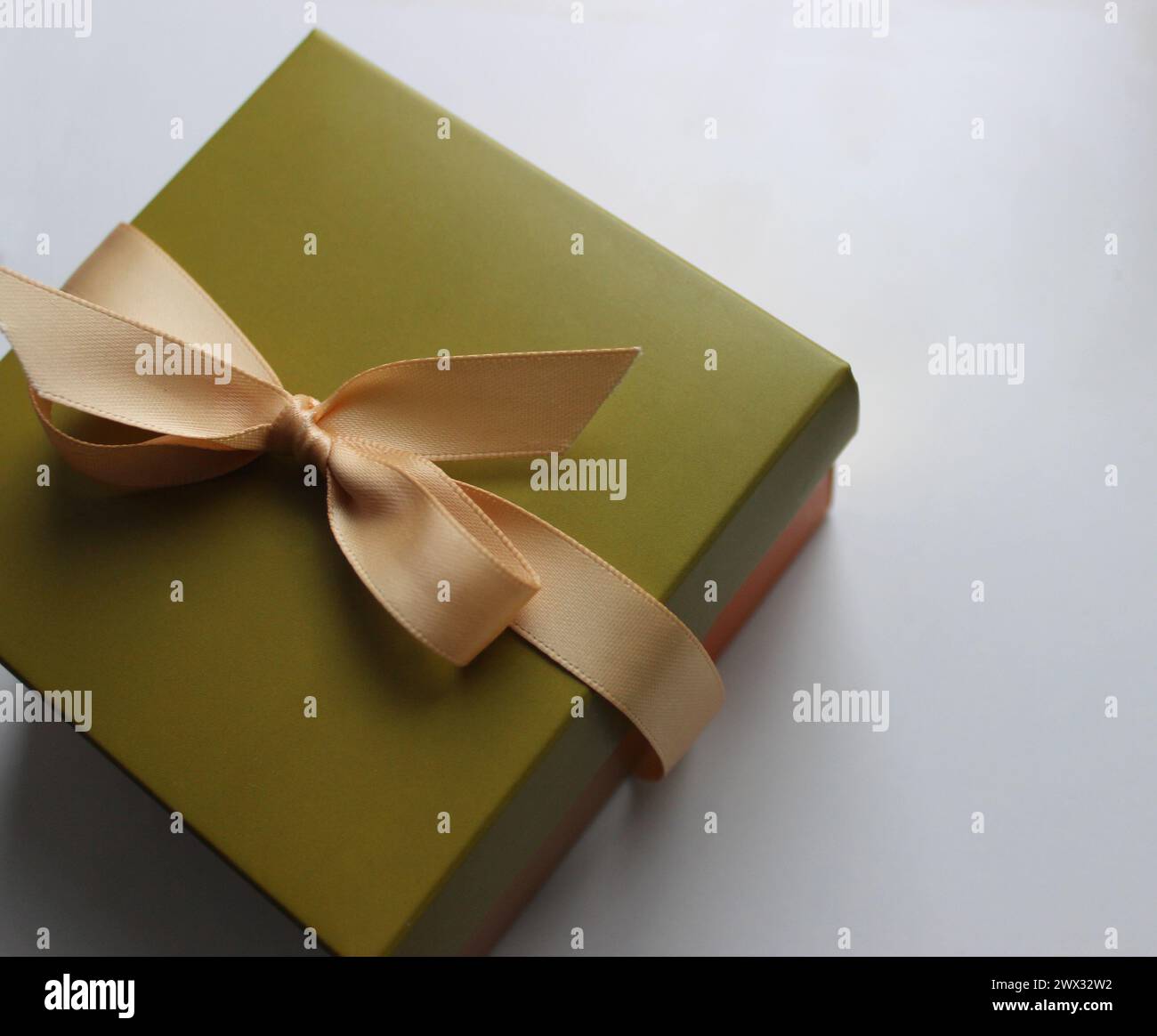 Confezione regalo in tonalità oliva con un elegante nastro beige su un foglio di carta bianco Foto Stock