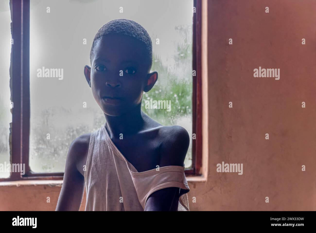 carestia in africa, ragazza triste e magra con corpo minuscolo e braccia magre, retroilluminazione dalla finestra di una stanza Foto Stock