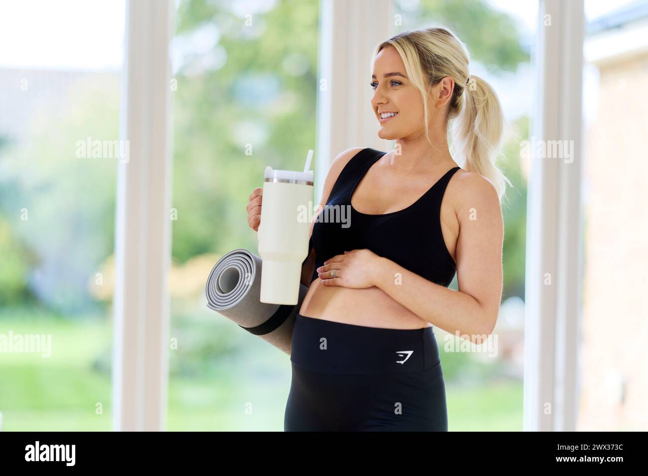 Donna incinta che porta il tappetino da yoga Foto Stock