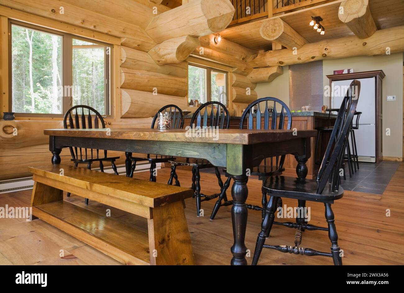 Tavolo da pranzo in legno antico colorato nero con sedie arrotondate con schienale alto e panca in legno di pino nella sala da pranzo open space e cucina interna Foto Stock