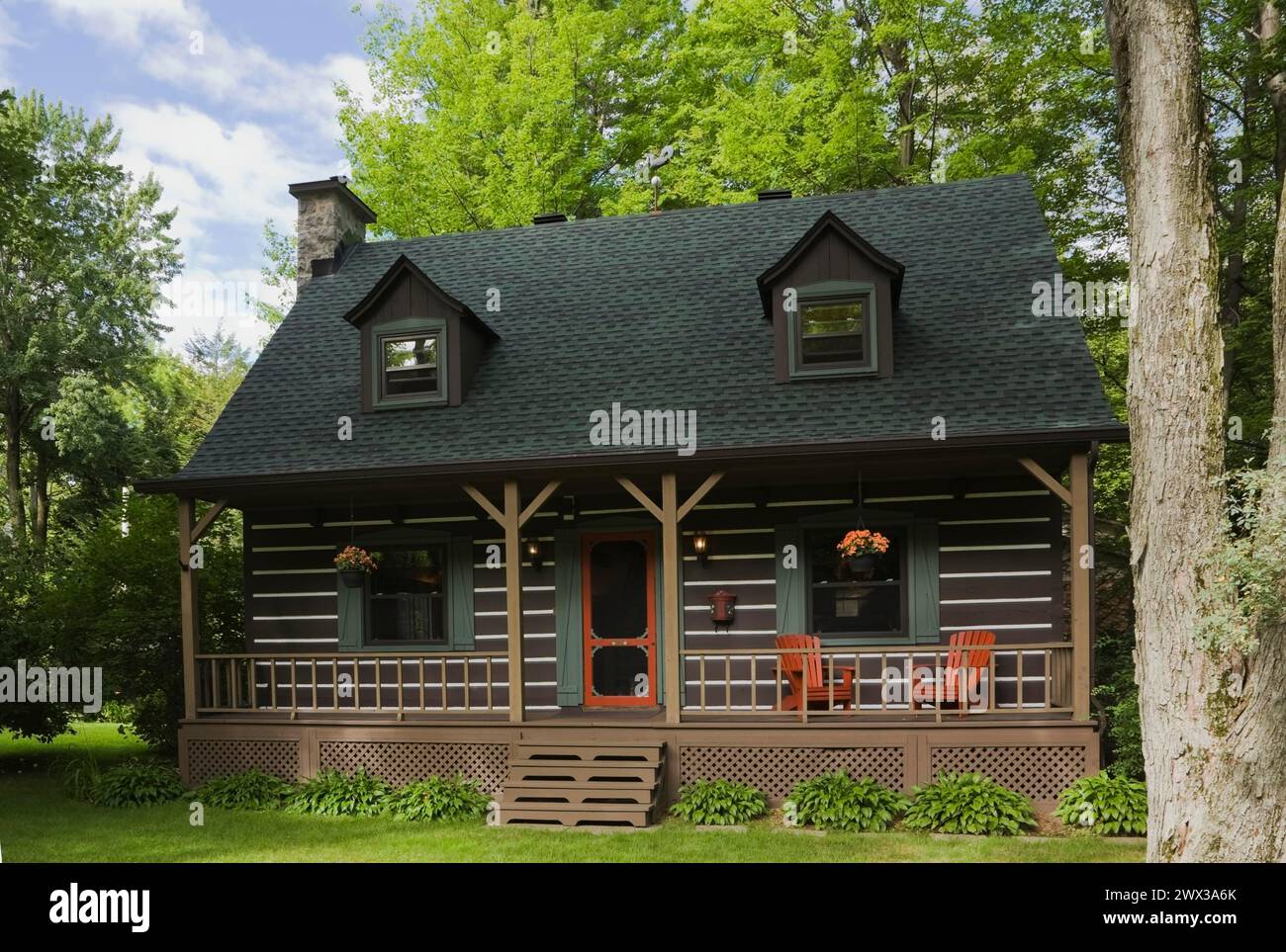 Facciata casalinga in stile cottage canadese di legno marrone a due piani con finiture verdi e rosse con lunga veranda in estate, Quebec, Canada Foto Stock