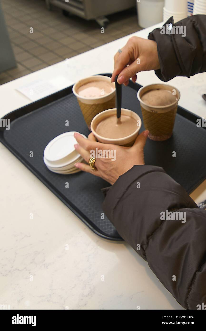 Presso il bancone di una caffetteria, una mano tiene un vassoio con tre tazze da caffè, che riflettono la routine quotidiana della città e la necessità di una carica energetica. Foto Stock