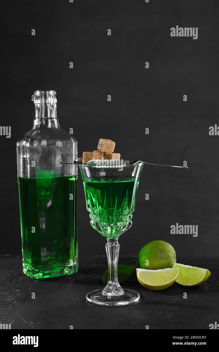 Absinthe, zucchero di canna e lime sul tavolo nero. Bevanda alcolica Foto Stock