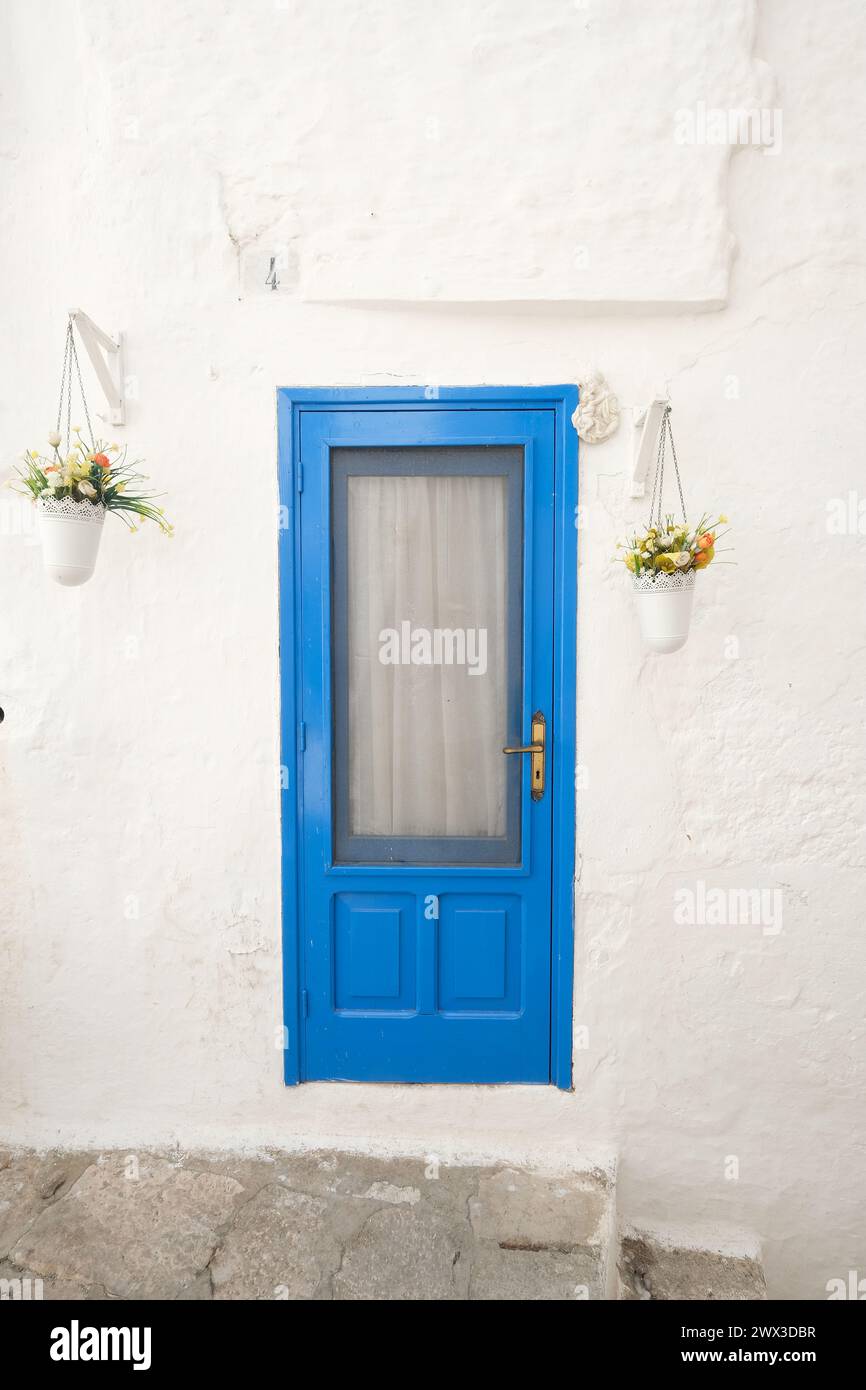 Porta blu vivace su un muro bianco in Puglia, italia, adornata da vasi di fiori appesi Foto Stock