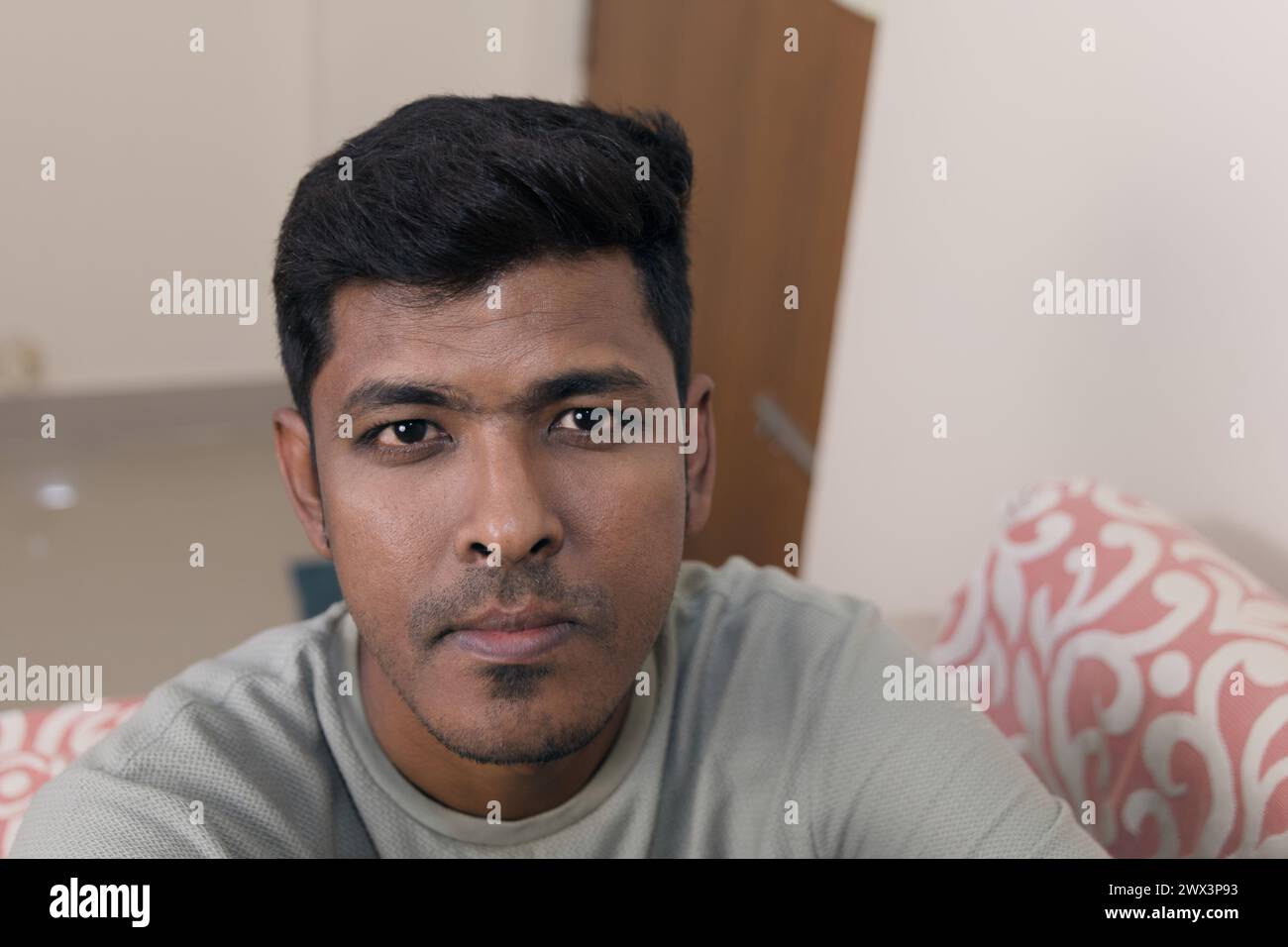 Un uomo indiano premuroso siede su un divano, guardando direttamente lo spettatore con un'espressione seria Foto Stock