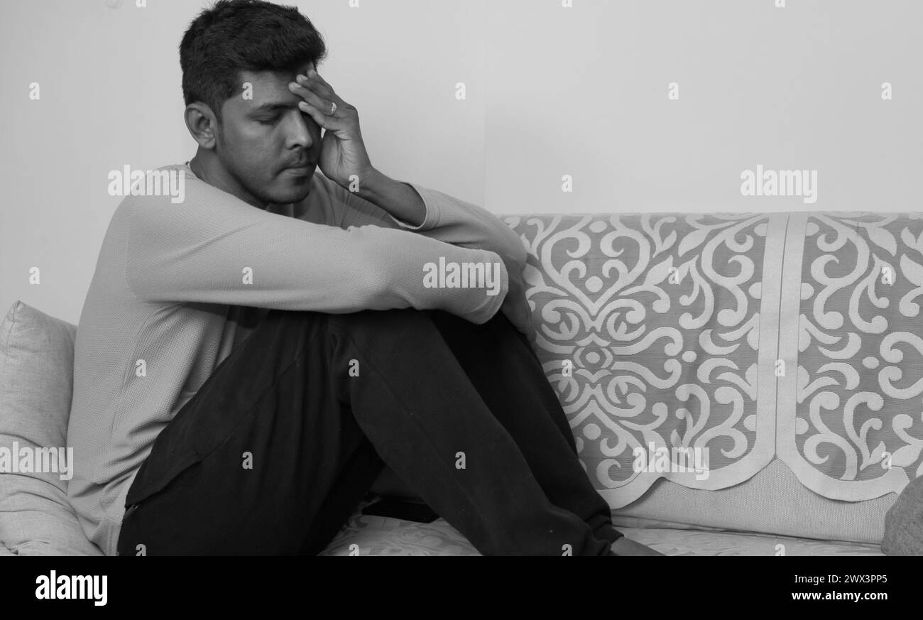 Una foto in bianco e nero di un giovane affondato nel pensiero su un divano, il suo linguaggio del corpo che trasmette sentimenti di solitudine e di reiezione Foto Stock
