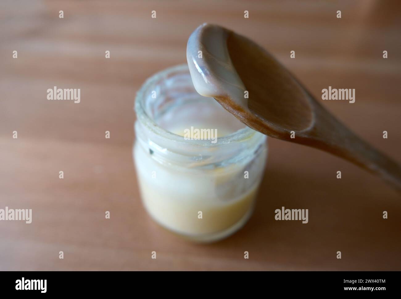 Gelatina reale in un piccolo barattolo. Si chiama anche latte d'api. Concentrata sulla goccia nel cucchiaio di legno. Foto Stock