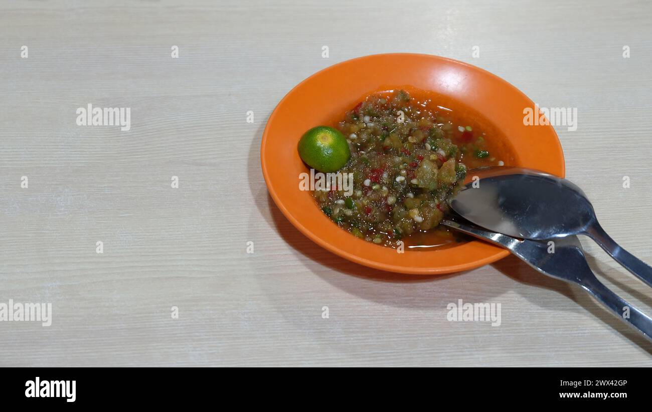 Un piatto di salsa con condimento di salsa di soia al peperoncino, con un calamansi a lato, e un paio di forchetta di metallo e cucchiaio. Con spazio di copia a sinistra. Foto Stock