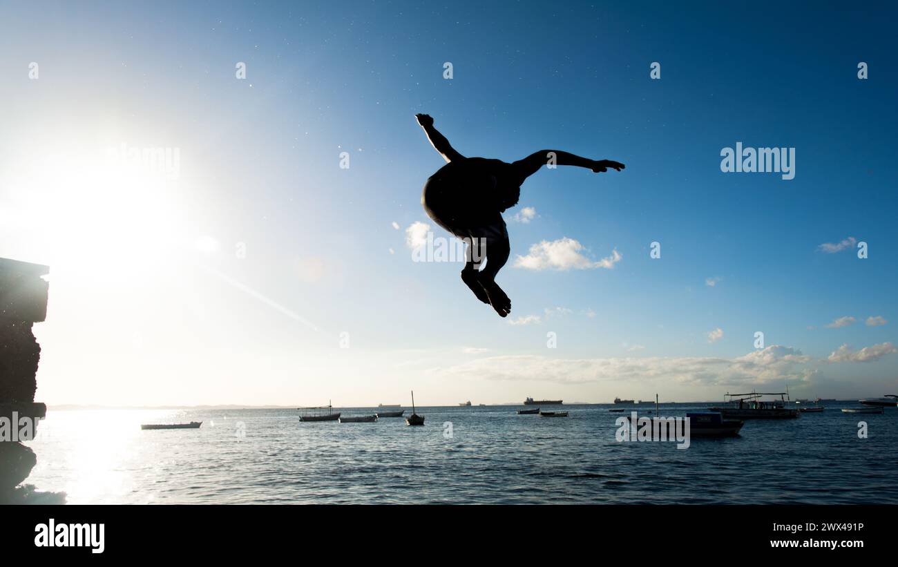 Salvador, Bahia, Brasile - 31 maggio 2019: Giovane nativo, in silhouette, salta dal molo di Porto da barra nella città di Salvador, Bahia. Foto Stock