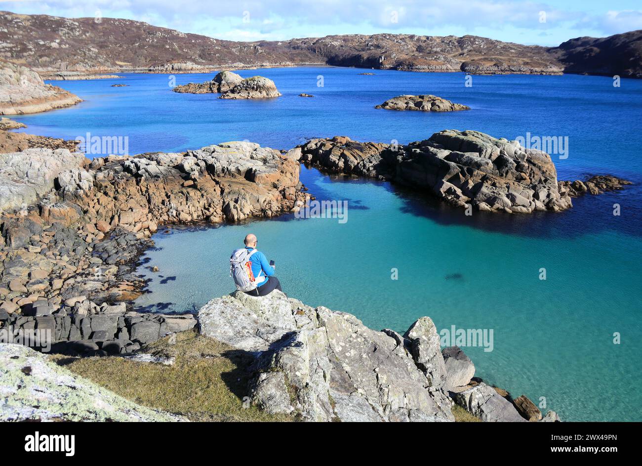 Isola di Mull, uomo seduto su rocce che si affaccia sul bellissimo mare limpido di Port na Ron, una remota baia sul Ross di Mull, Scozia Foto Stock