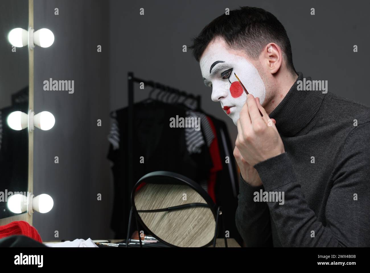 Giovane che applica il trucco mimo vicino allo specchio nello spogliatoio Foto Stock