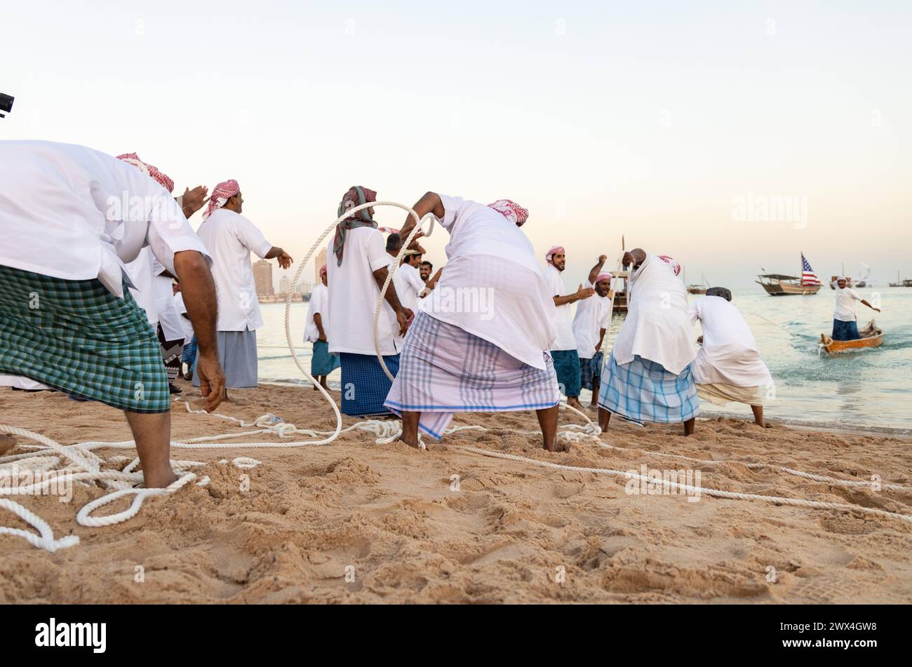 Pescatori arabi non identificati tirano la loro sciabica fuori dal mare sulla spiaggia di katara, Doha, Qatar. La pesca è ancora la principale fonte di reddito per la gente del posto. Foto Stock