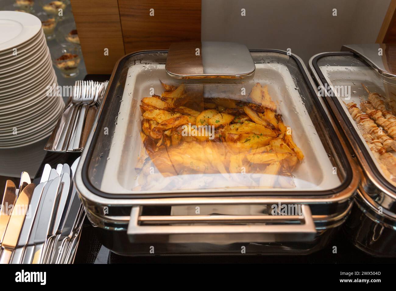 Le patate fritte si guarniscono in uno scaldavivande su un tavolo a buffet in un ristorante dell'hotel. Tavolo con stoviglie e luccicanti marmiti in attesa degli ospiti. Foto Stock