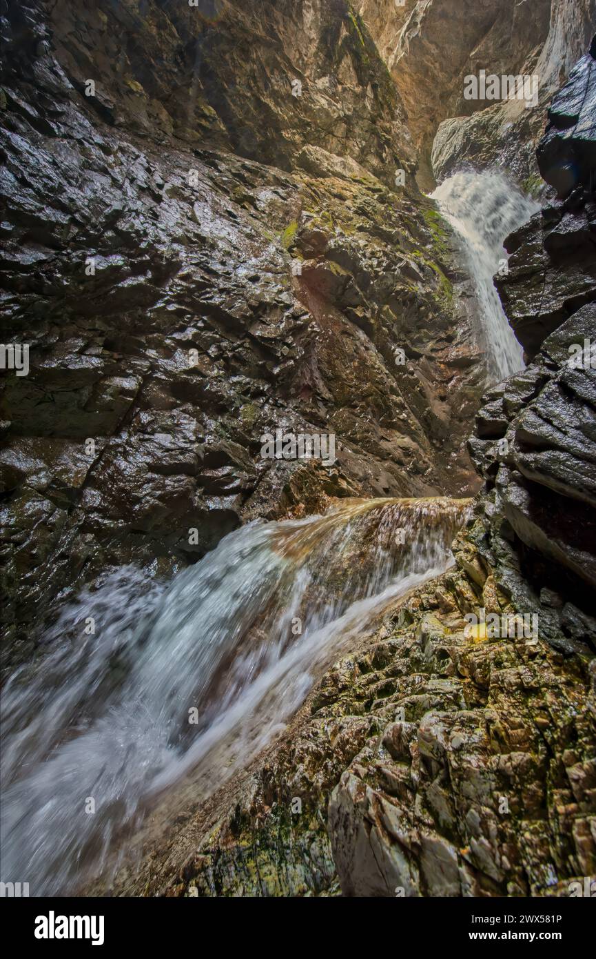 Il potente flusso di una cascata attraversa una profonda gola rocciosa circondata da scintillanti pietre bagnate Foto Stock