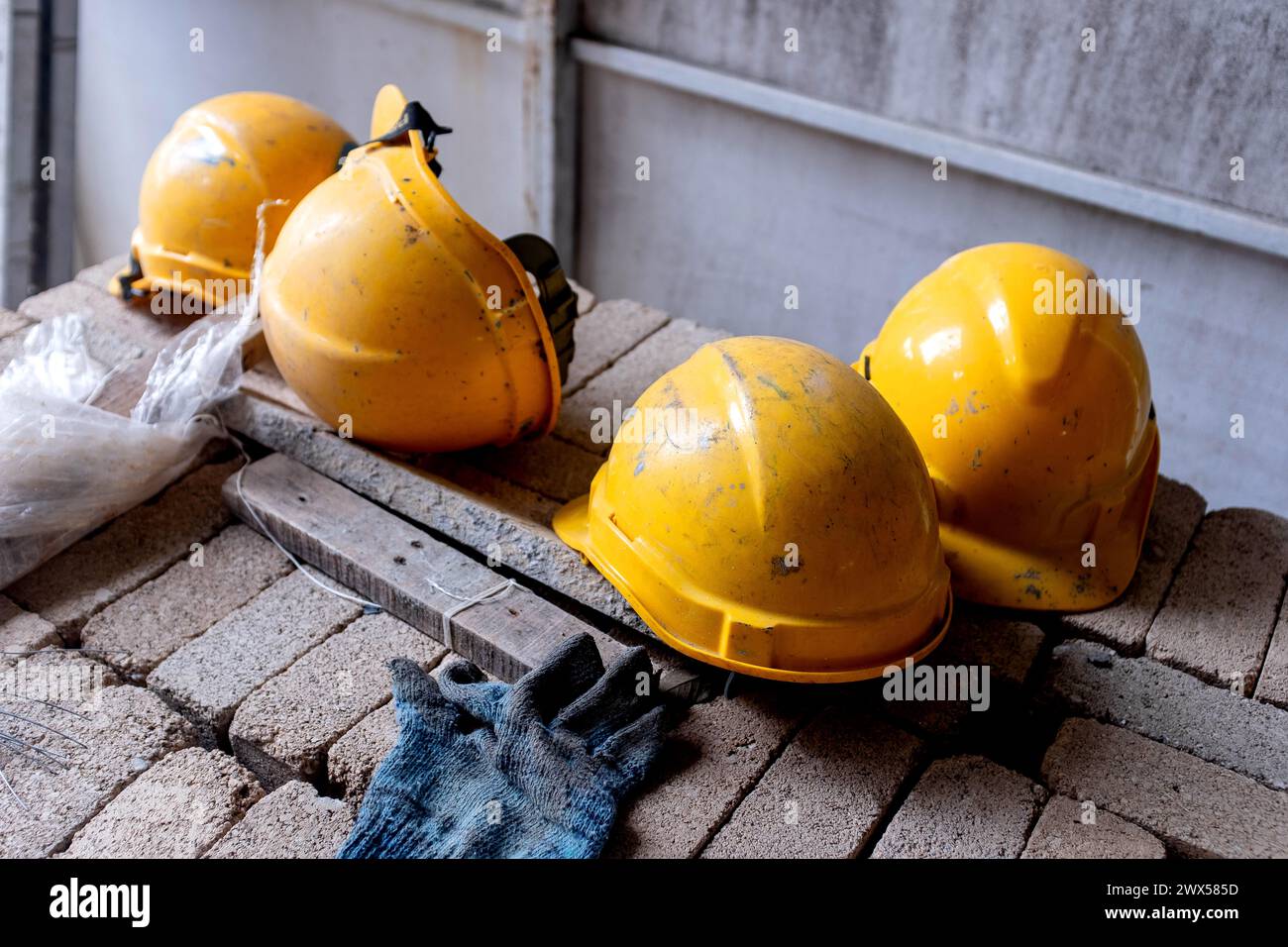 Cappelli rigidi gialli di sicurezza adagiati su un mucchio di mattoni in un cantiere edile. Foto Stock