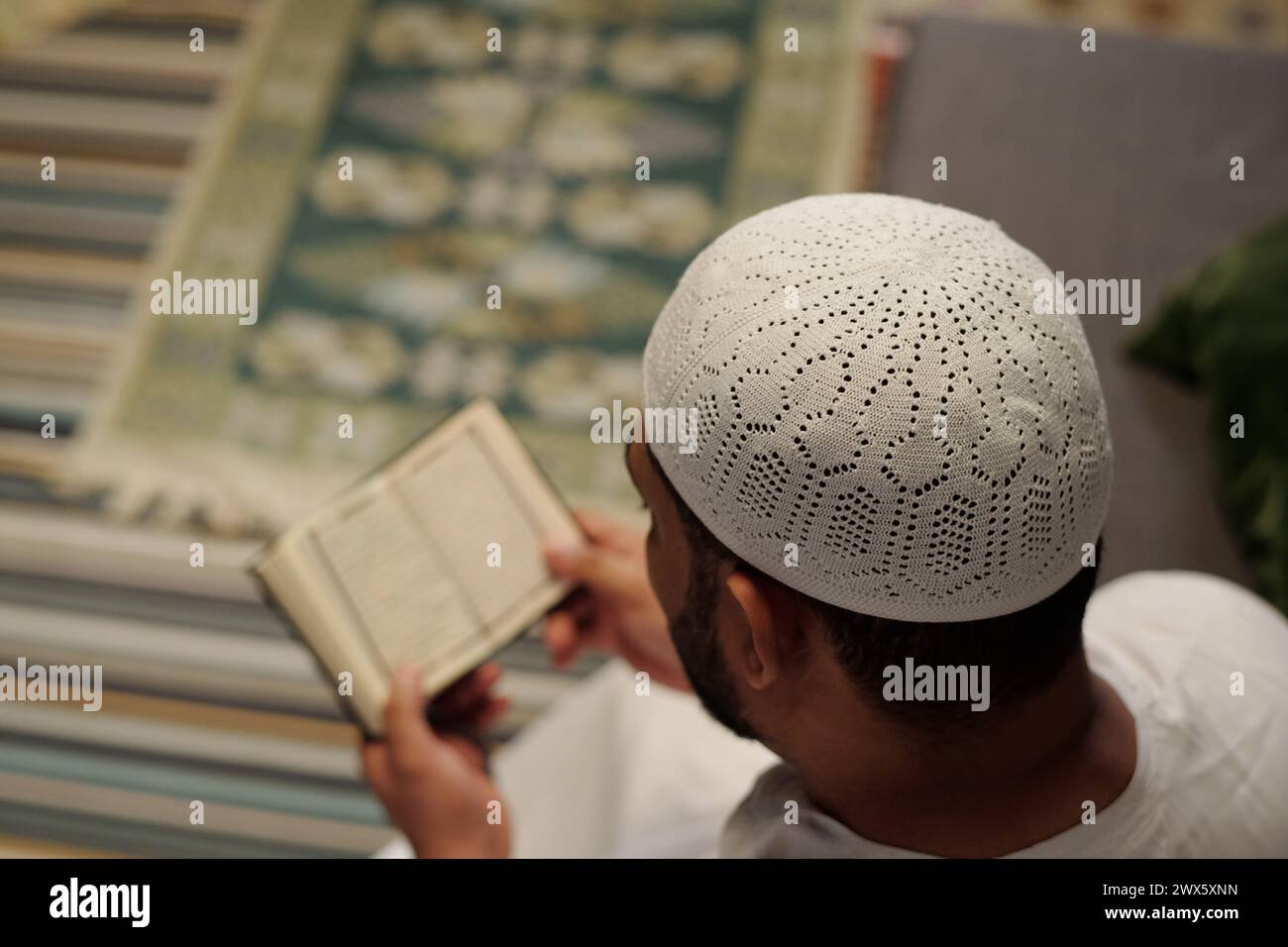 Ripresa selettiva con vista ad alto angolo dell'irriconoscibile uomo musulmano che indossa taqiyah bianca che legge il Corano, copia spazio Foto Stock