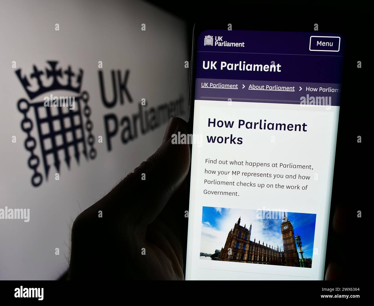 Persona che detiene un cellulare con pagina web dell'organo legislativo Parlamento del Regno Unito (UK) con logo. Messa a fuoco al centro del display del telefono. Foto Stock