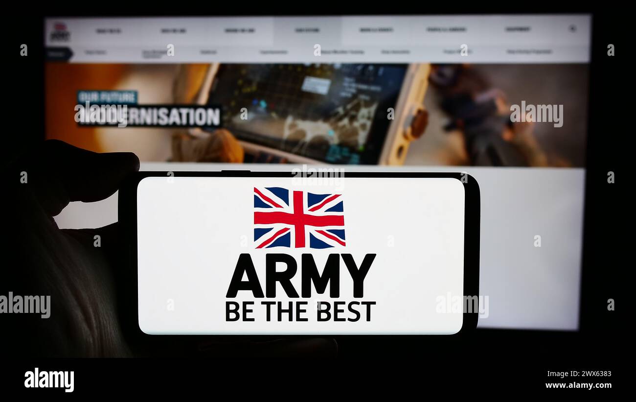 Persona che detiene un cellulare con il logo della forza di terra britannica British Army davanti alla pagina web. Mettere a fuoco il display del telefono. Foto Stock