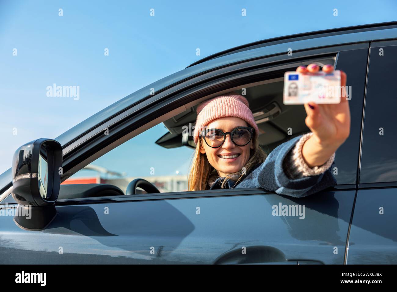 donna sorridente che mostra la sua nuova patente fuori dal finestrino dell'auto nella giornata di sole Foto Stock