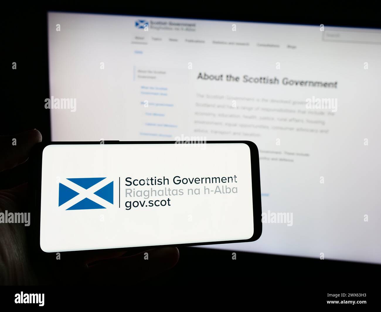Persona che possiede uno smartphone con il logo del governo scozzese (Riaghaltas na h-Alba) davanti al sito web. Mettere a fuoco il display del telefono. Foto Stock