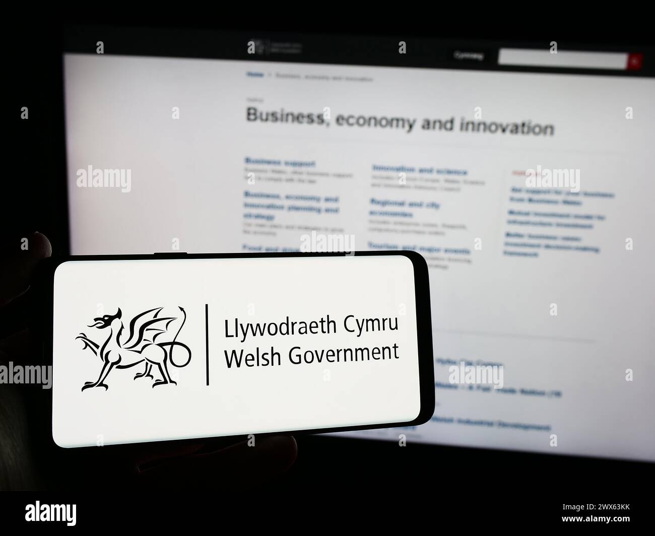 Persona con smartphone con logo del governo gallese (Llywodraeth Cymru) davanti al sito Web. Mettere a fuoco il display del telefono. Foto Stock