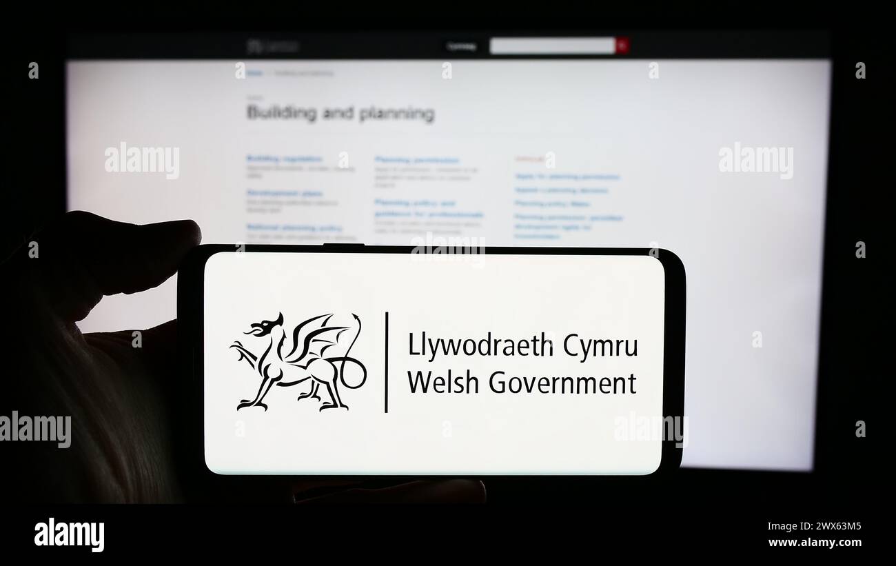 Persona che detiene un cellulare con il logo del governo gallese (Llywodraeth Cymru) davanti alla pagina web. Mettere a fuoco il display del telefono. Foto Stock