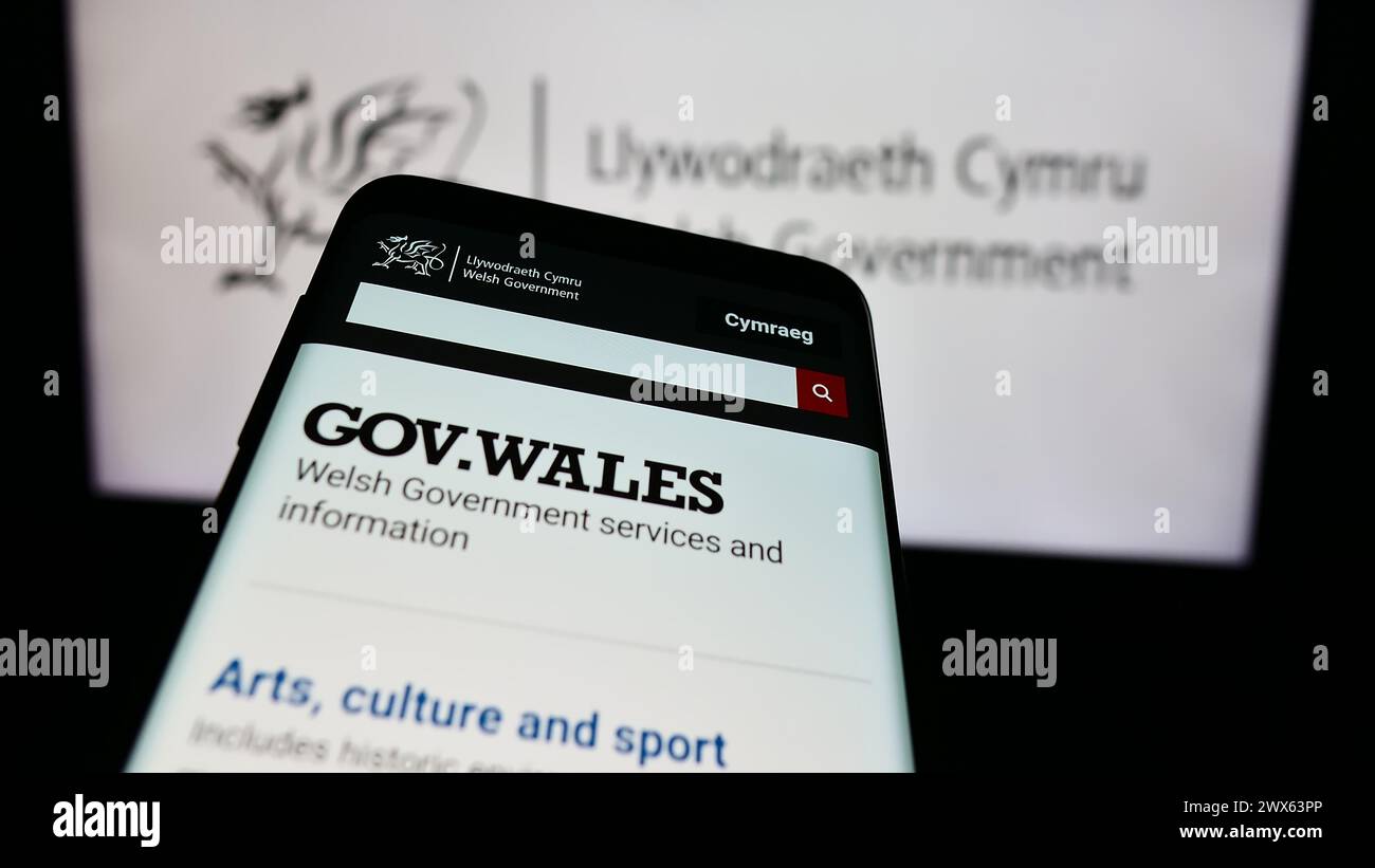 Telefono cellulare con sito web del governo gallese (Llywodraeth Cymru) davanti al logo. Mettere a fuoco in alto a sinistra sul display del telefono. Foto Stock
