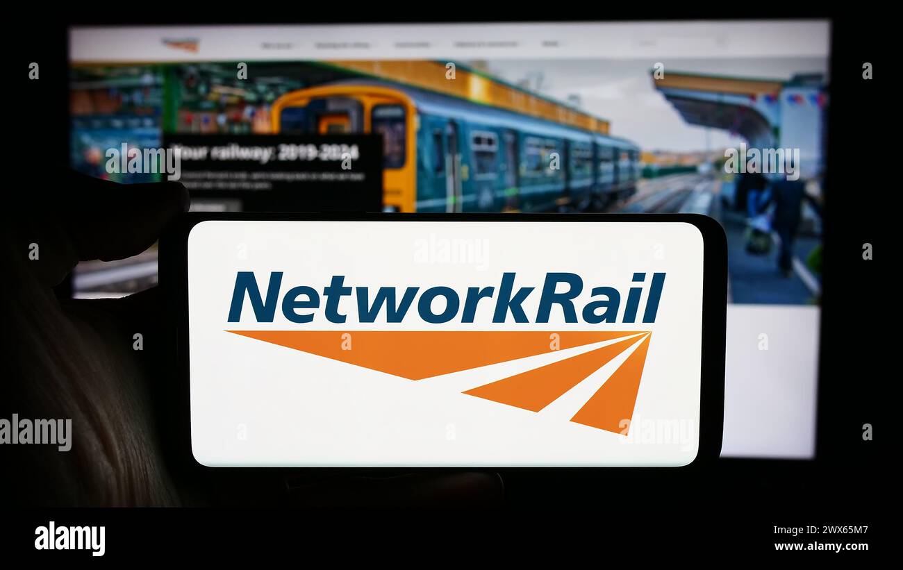 Persona che detiene un cellulare con il logo della società di infrastrutture ferroviarie Network Rail Limited di fronte alla pagina web aziendale. Mettere a fuoco il display del telefono. Foto Stock