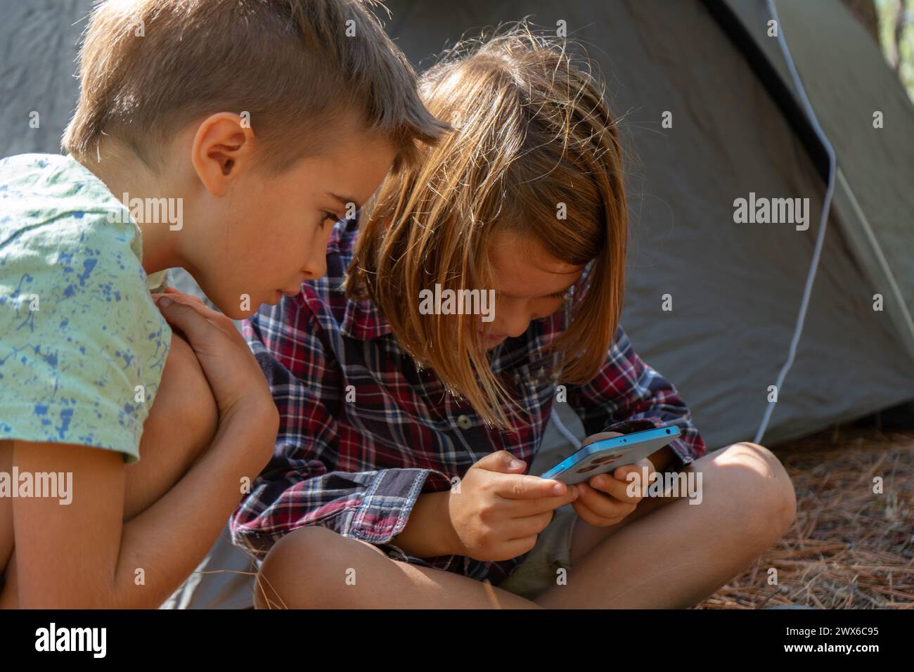 Bambini in campeggio nella foresta che giocano con lo smartphone Foto Stock