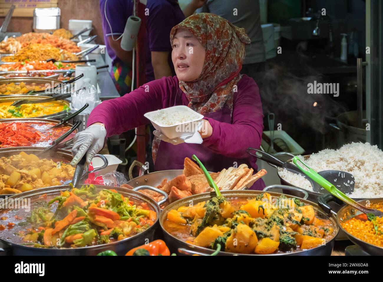 Londra, Regno Unito - 12 settembre 2023 - Una donna musulmana asiatica che serve piatti da asporto al curry al mercato alimentare di Camden Foto Stock