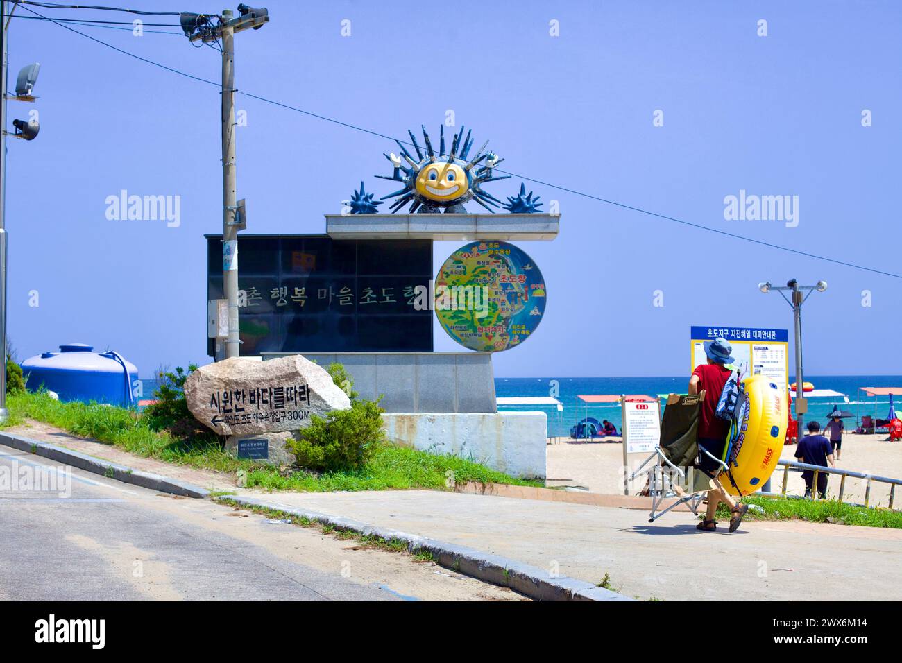 Contea di Goseong, Corea del Sud - 31 luglio 2019: All'estremità nord della spiaggia di Hwajinpo, un visitatore si prepara per una giornata al mare, passando un cartello di granito con Foto Stock