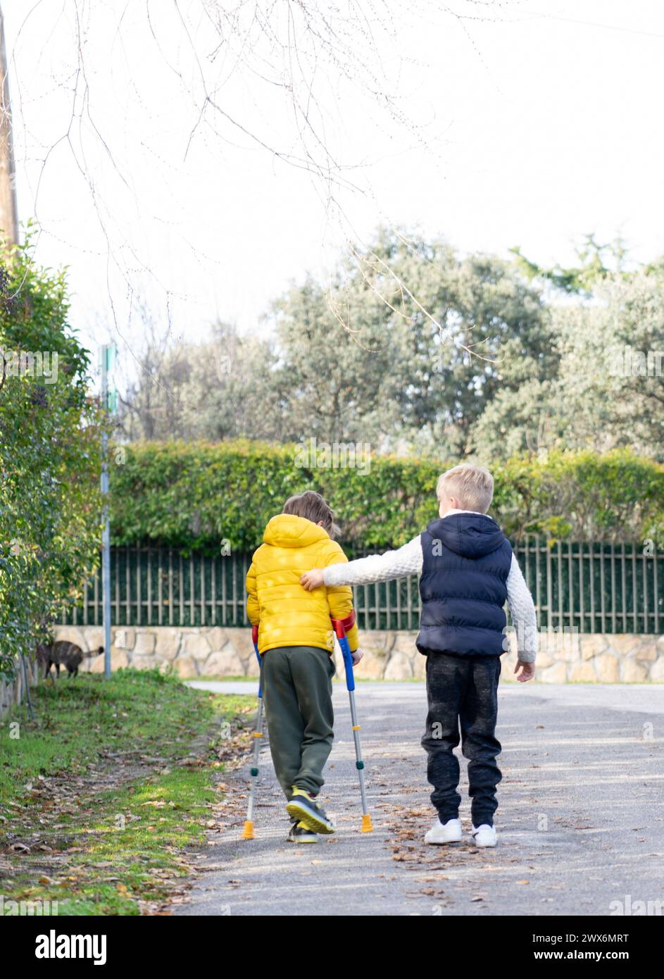 Ragazzo con le stampelle che cammina per strada con il suo amico Foto Stock