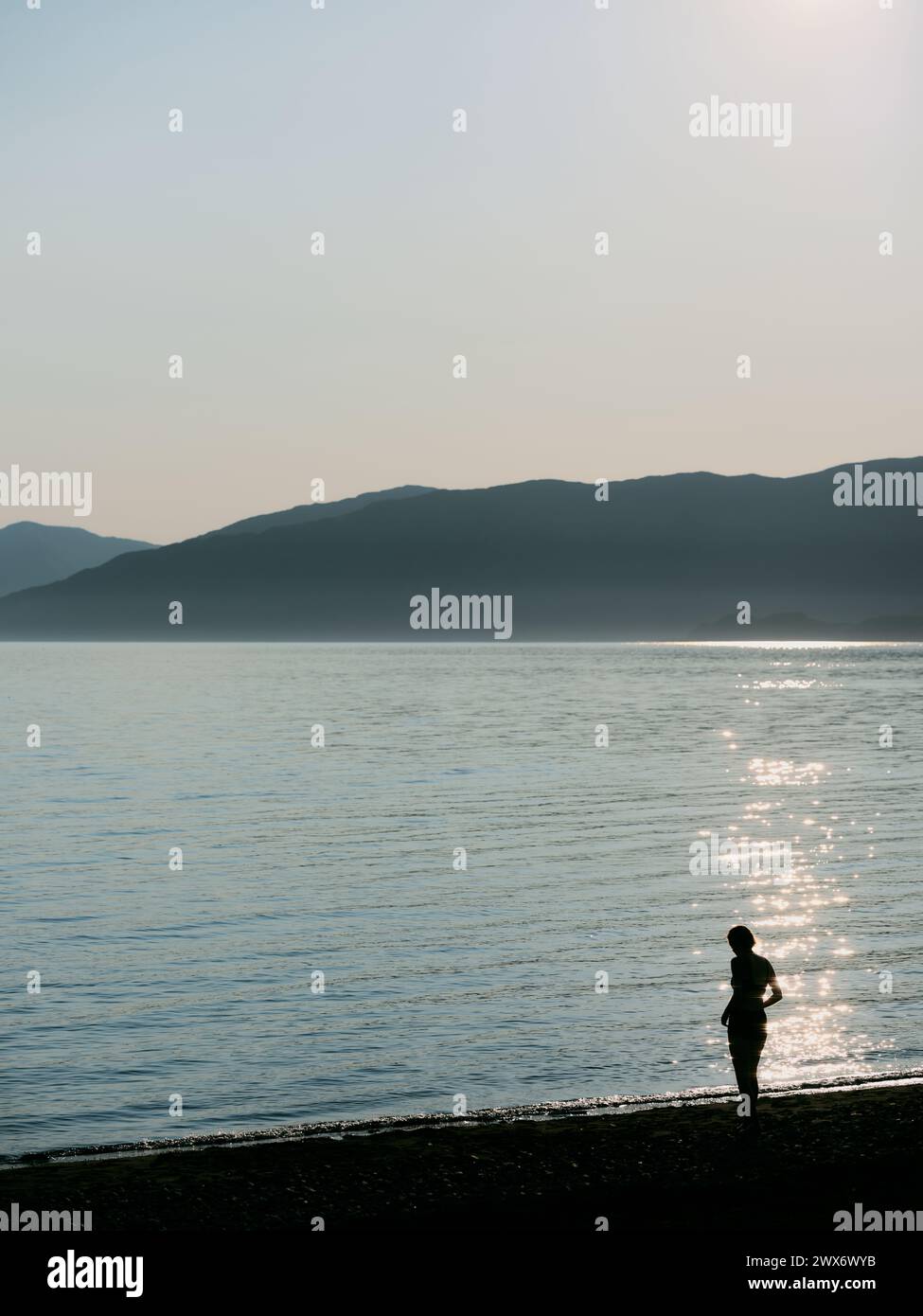 Una figura dalla silhouette solitaria retroilluminata contro il sole sulla costa - libertà all'aperto paesaggio marino Foto Stock