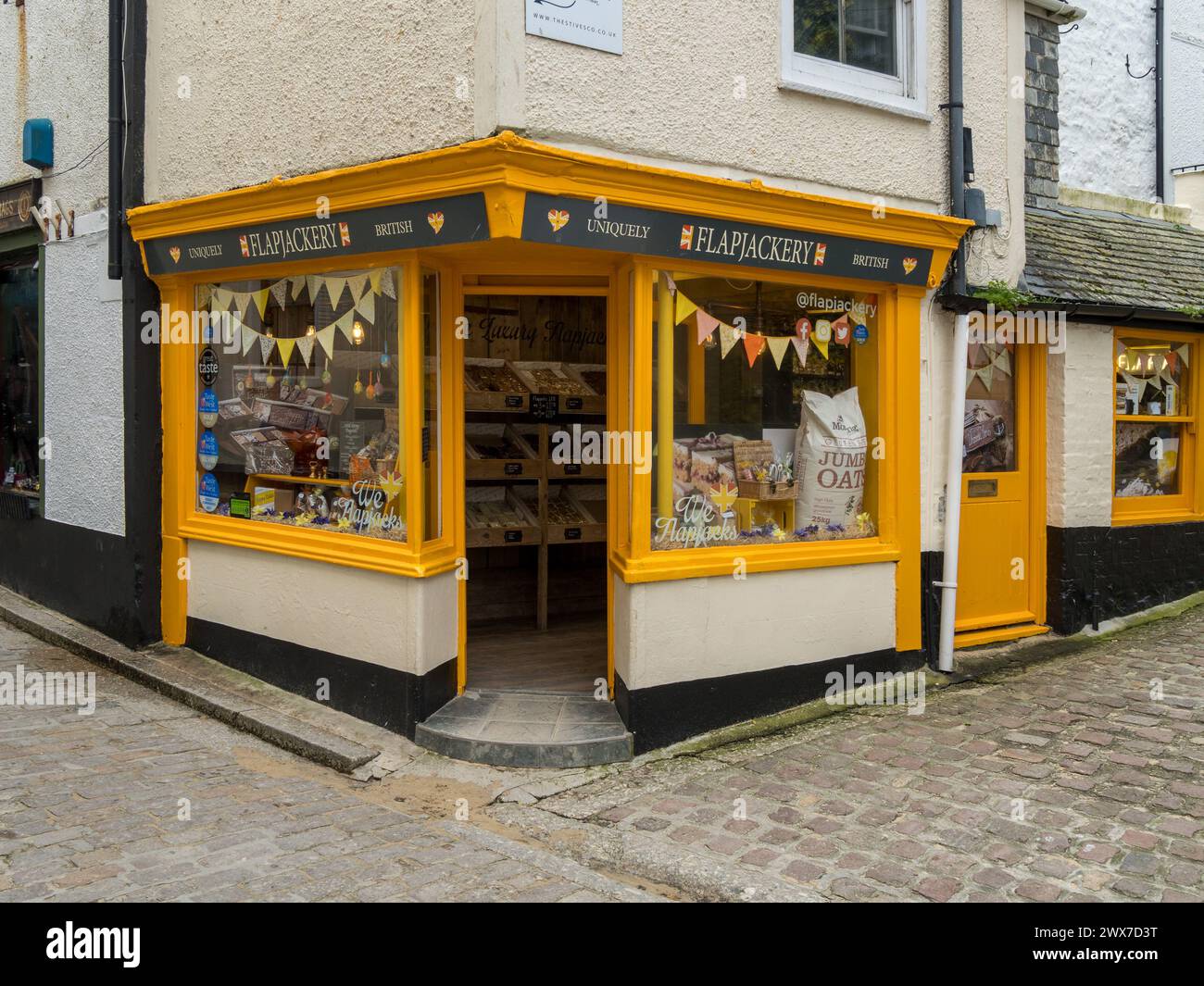 Vetrina gialla luminosa di un tradizionale negozio di flapjackery con vetrine in una strada acciottolata, St Ives, Cornovaglia, Inghilterra, Regno Unito Foto Stock