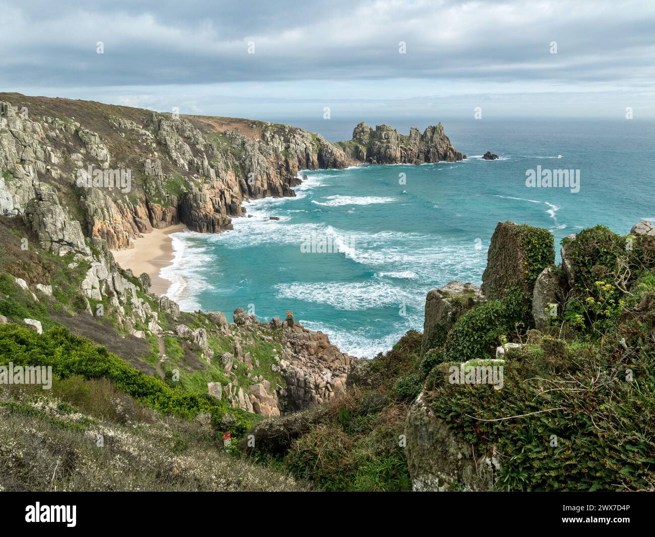 La spiaggia di Pedn Vounder e il promontorio di Logan Rock sono visti dal sentiero costiero della Cornovaglia meridionale vicino a Porthcurno in Spring, Cornovaglia, Inghilterra, Regno Unito Foto Stock