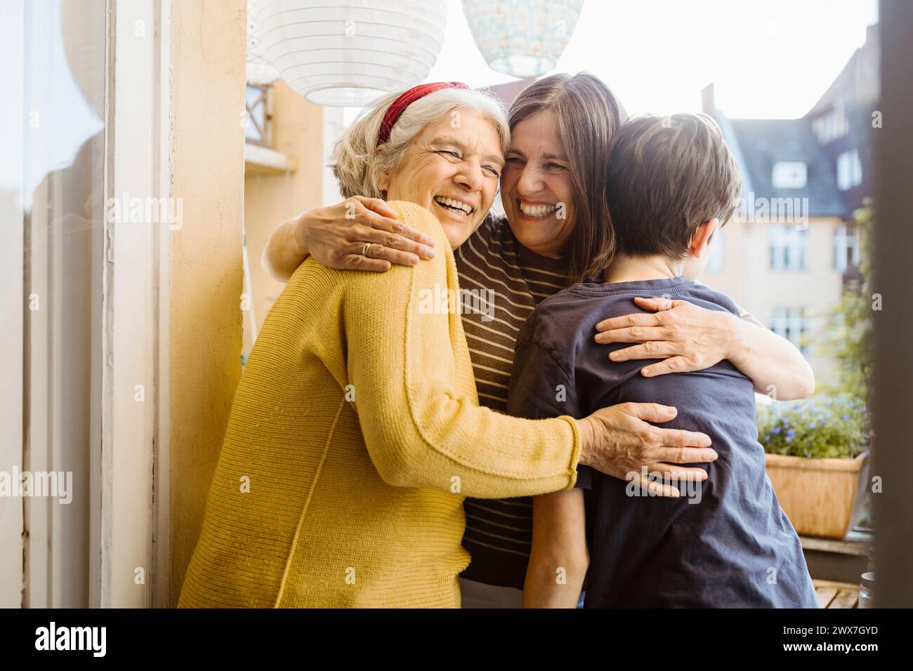 Donna felice che abbraccia la suocera e il figlio mentre si trova in balcone Foto Stock