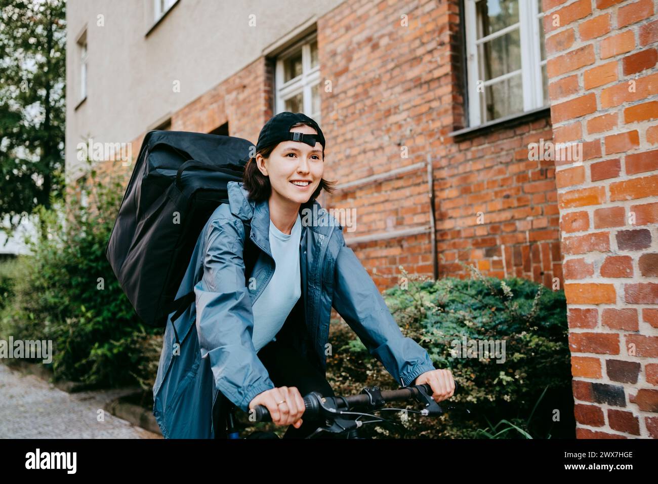 Motociclista sorridente che fa la consegna in bicicletta in strada in città Foto Stock