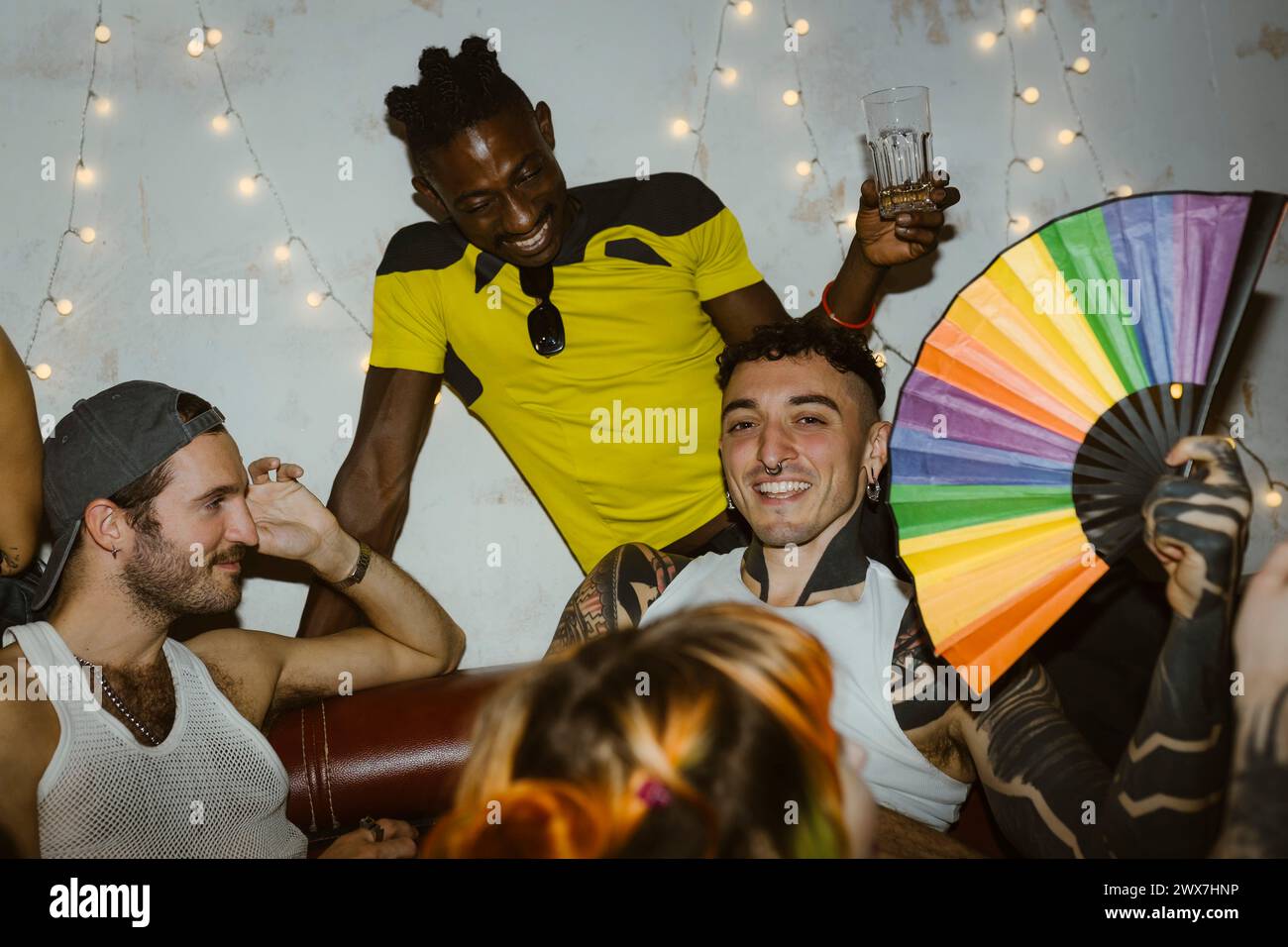 Ritratto di una persona sorridente che tiene in mano un ventilatore multicolore mentre si diverte con gli amici al nightclub Foto Stock