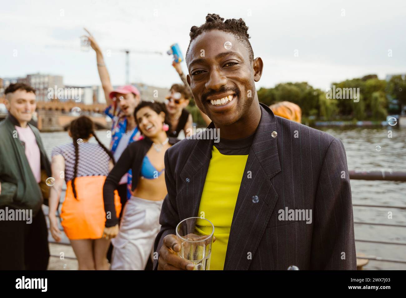 Ritratto di una persona sorridente che regge un bicchiere da bere con gli amici sullo sfondo Foto Stock Ritratto di una persona sorridente che regge un bicchiere da bere con gli amici sullo sfondo Foto Stock