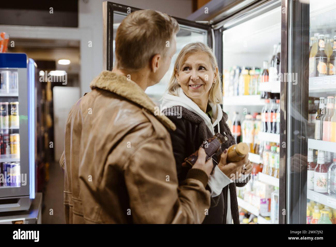 Donna sorridente che guarda l'uomo mentre compra bevande dalla sezione refrigerata del supermercato Foto Stock