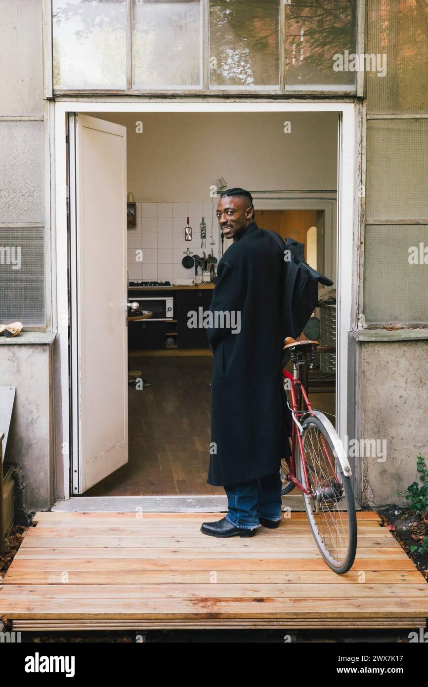 Uomo d'affari in soprabito con la bicicletta in piedi fuori dal luogo di lavoro Foto Stock